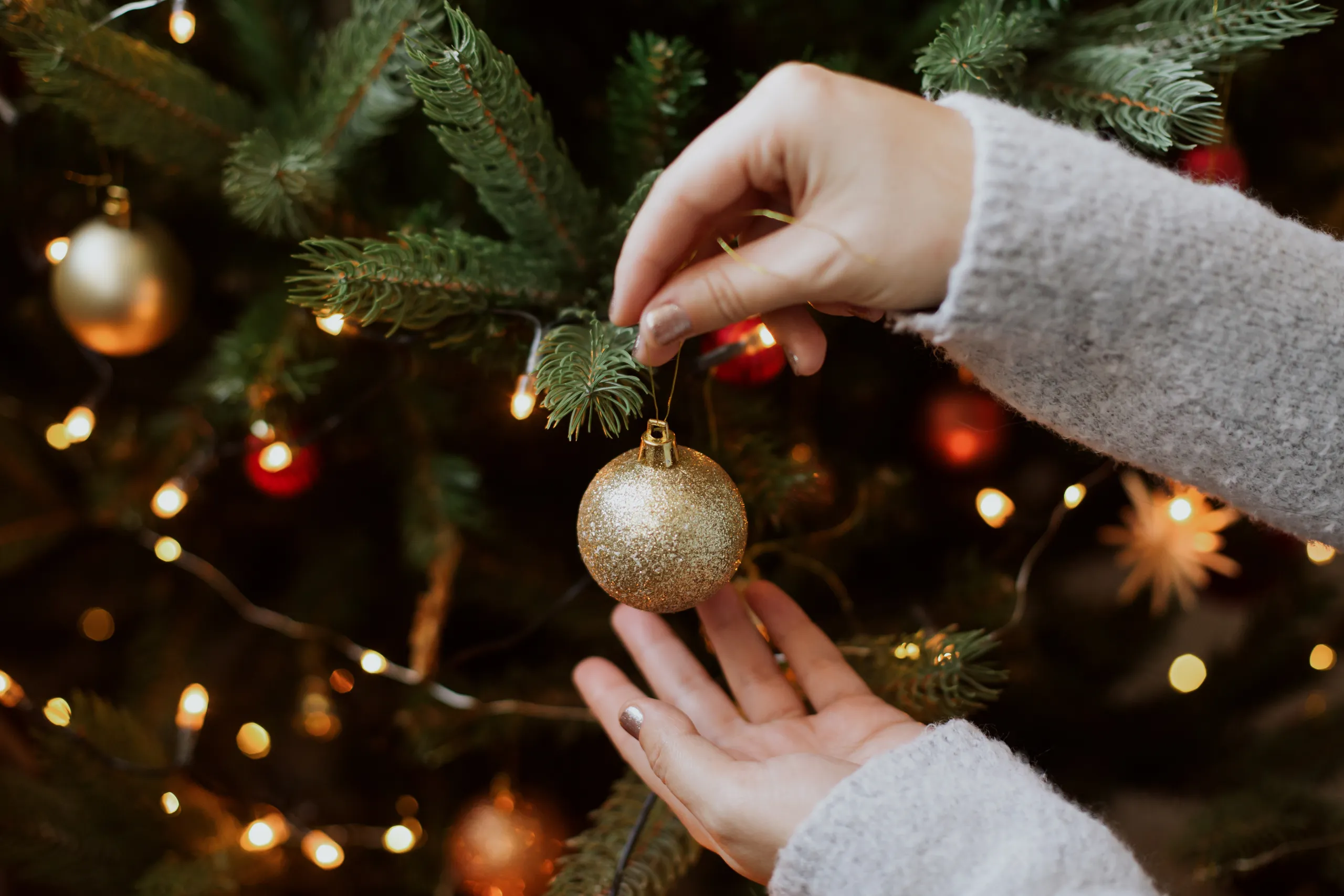 pessoa colocando bola de natal em árvore de natal