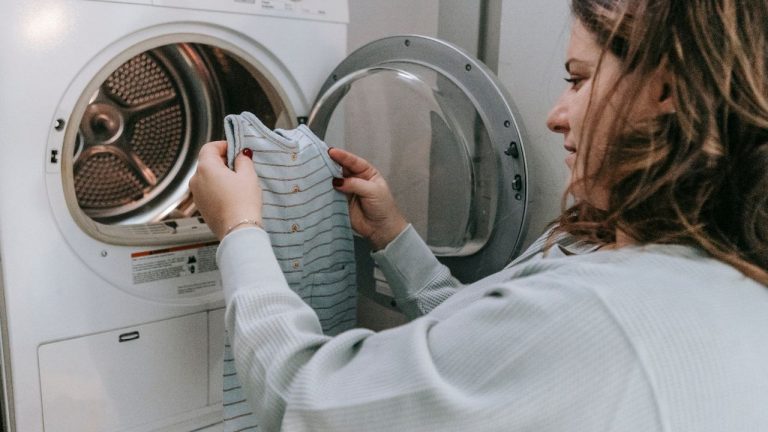 mulher olhando roupa em frente à máquina de lavar